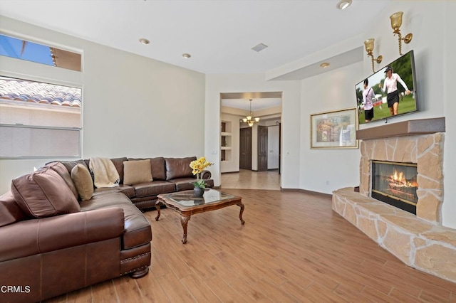 living room featuring a stone fireplace, wood-type flooring, and a notable chandelier