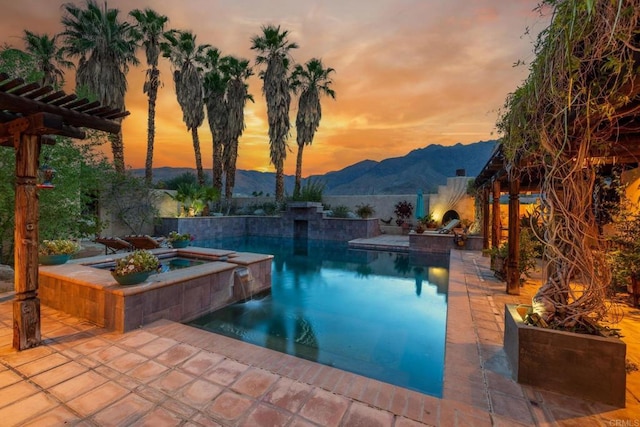 pool at dusk featuring a patio, a mountain view, and an in ground hot tub