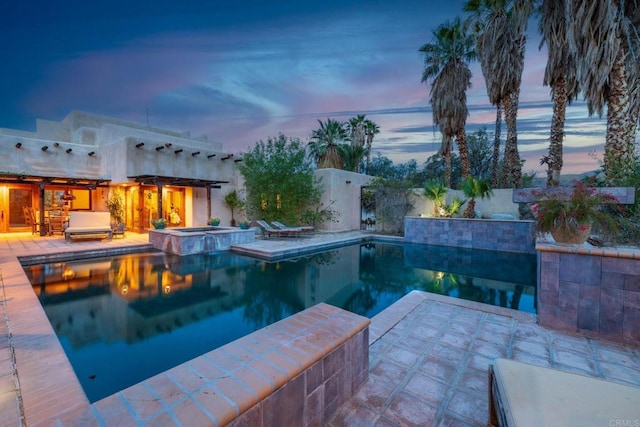 pool at dusk featuring a patio and an in ground hot tub