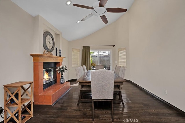 dining space featuring dark hardwood / wood-style floors, ceiling fan, high vaulted ceiling, and a tiled fireplace