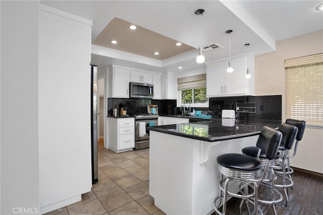 kitchen with hanging light fixtures, stainless steel appliances, a kitchen breakfast bar, kitchen peninsula, and white cabinets