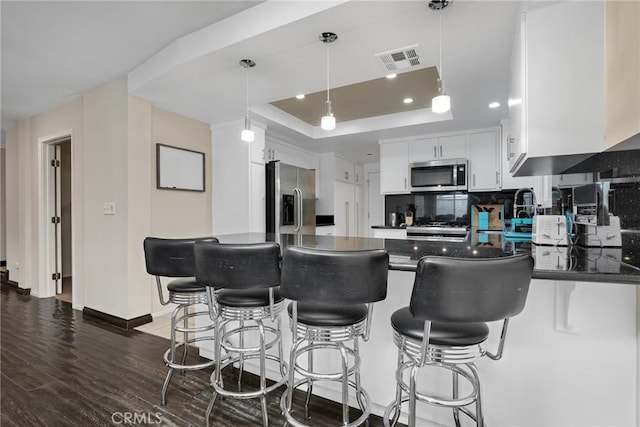 kitchen featuring dark wood-type flooring, white cabinets, a tray ceiling, decorative light fixtures, and stainless steel appliances