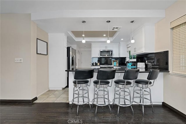 kitchen featuring kitchen peninsula, appliances with stainless steel finishes, a raised ceiling, decorative light fixtures, and white cabinetry