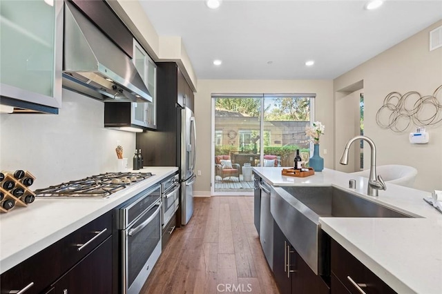 kitchen featuring stainless steel appliances, sink, dark wood-type flooring, and wall chimney range hood