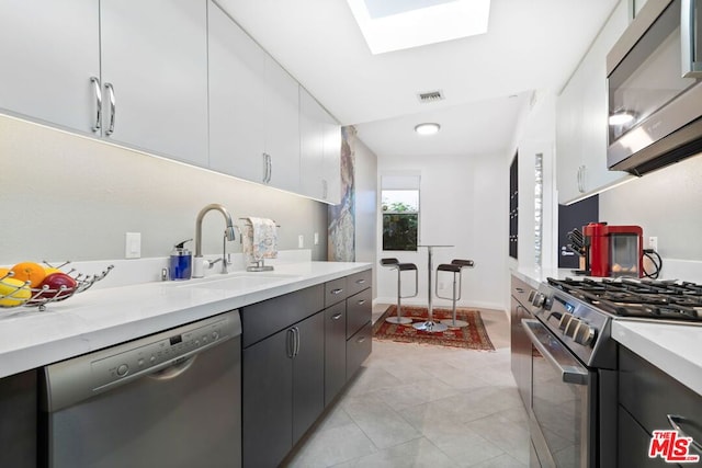 kitchen featuring a skylight, sink, stainless steel appliances, and white cabinetry