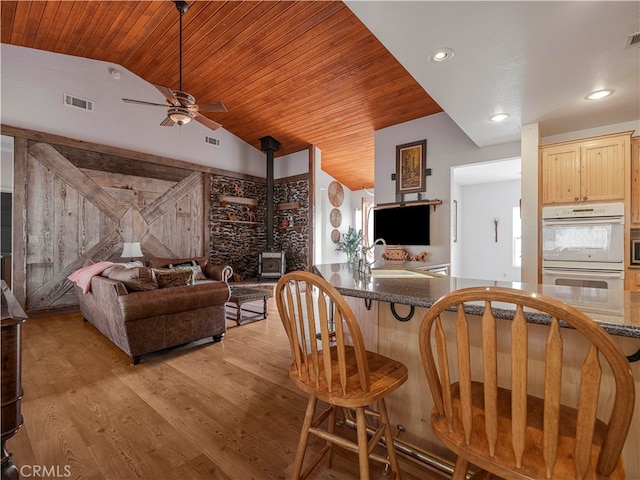 kitchen with lofted ceiling, light brown cabinets, light hardwood / wood-style flooring, a wood stove, and white double oven