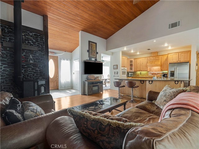 living room featuring light hardwood / wood-style flooring, high vaulted ceiling, a wood stove, and wood ceiling