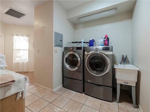 laundry area with electric panel, washer and clothes dryer, and light tile patterned floors