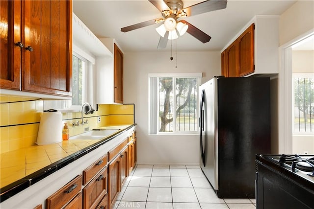 kitchen featuring stainless steel fridge, tile counters, a healthy amount of sunlight, light tile patterned flooring, and sink