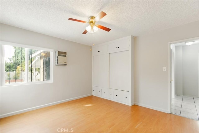 unfurnished bedroom featuring ceiling fan, a textured ceiling, light hardwood / wood-style flooring, and a wall unit AC