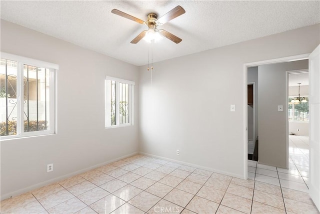 tiled spare room featuring a textured ceiling, a wealth of natural light, and ceiling fan with notable chandelier