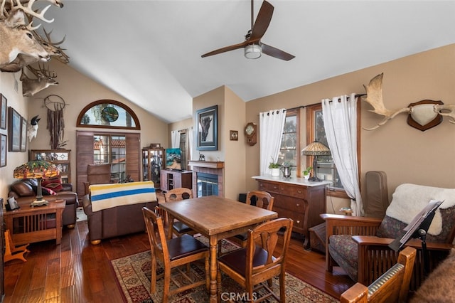 dining area featuring ceiling fan, dark wood-type flooring, a tile fireplace, and vaulted ceiling