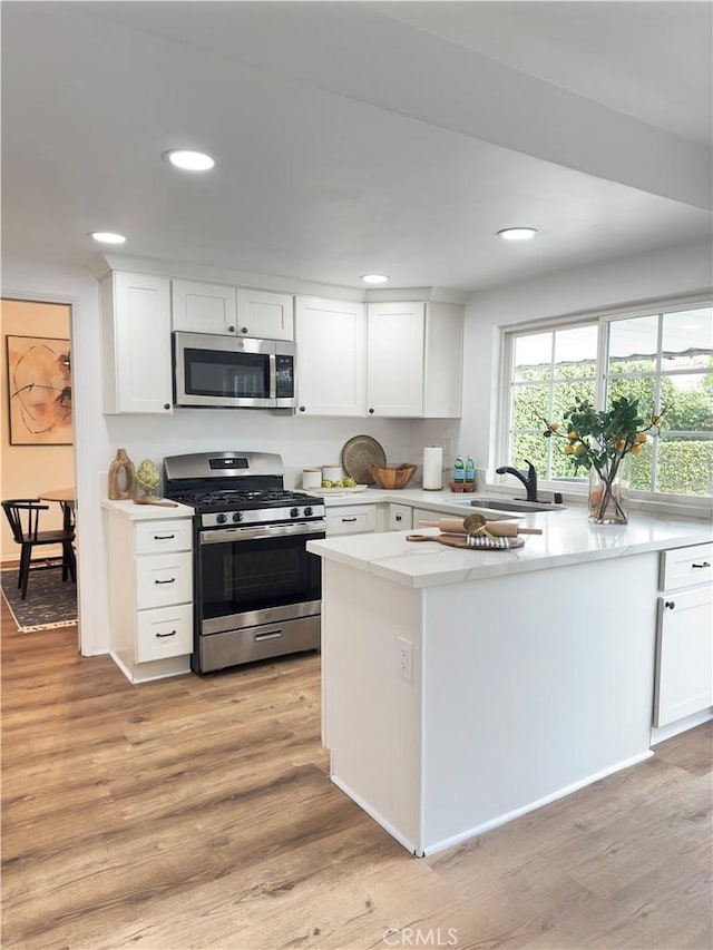 kitchen with kitchen peninsula, appliances with stainless steel finishes, sink, light hardwood / wood-style flooring, and white cabinetry