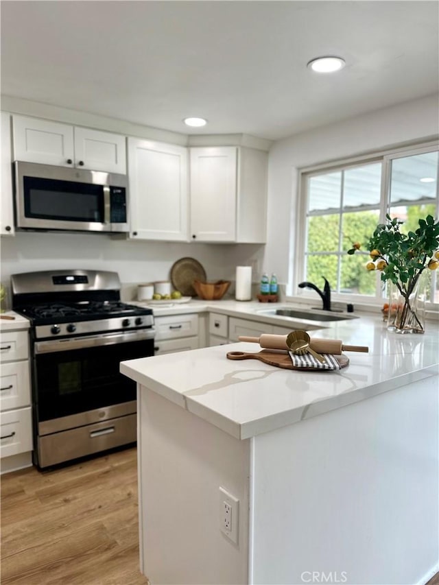 kitchen with light stone countertops, stainless steel appliances, sink, white cabinets, and light hardwood / wood-style floors