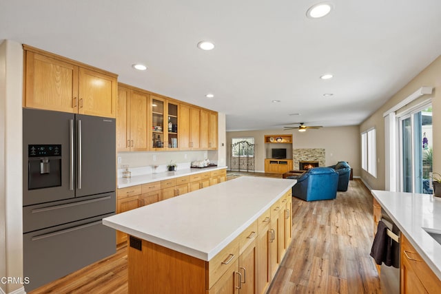 kitchen featuring light wood-type flooring, stainless steel appliances, ceiling fan, a center island, and a stone fireplace