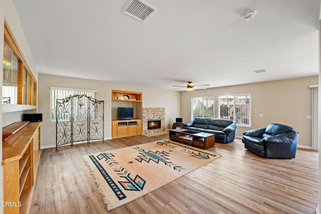 living room with hardwood / wood-style floors, a stone fireplace, and ceiling fan