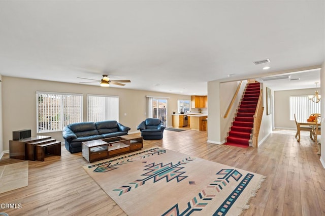 living area with stairs, visible vents, light wood-style floors, baseboards, and ceiling fan with notable chandelier