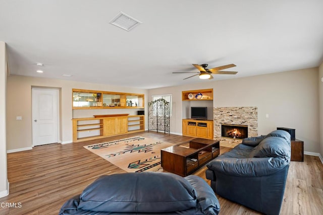 living room featuring built in shelves, a fireplace, visible vents, baseboards, and light wood finished floors