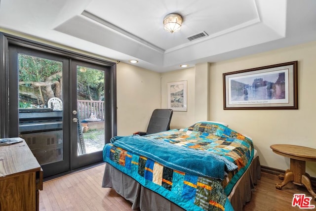 bedroom with access to outside, a tray ceiling, and light hardwood / wood-style floors