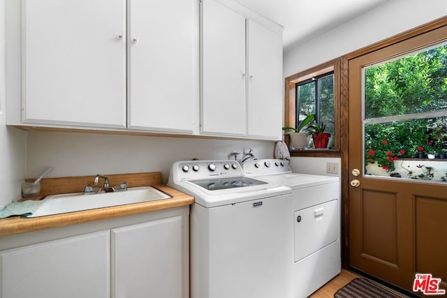 clothes washing area with washer and clothes dryer, sink, cabinets, and light wood-type flooring