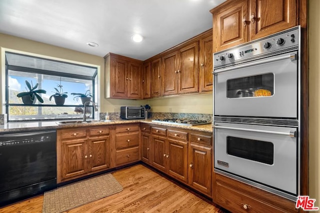 kitchen featuring light stone countertops, appliances with stainless steel finishes, light hardwood / wood-style flooring, and sink