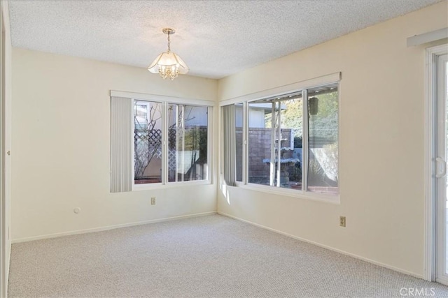 carpeted empty room featuring a textured ceiling and a notable chandelier