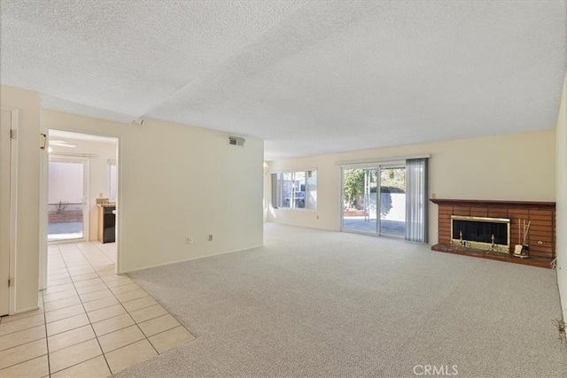 unfurnished living room with a brick fireplace, light colored carpet, and a textured ceiling