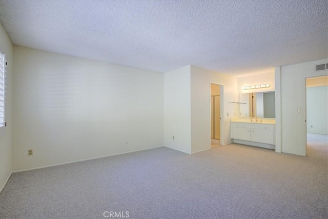 unfurnished bedroom featuring light carpet, a textured ceiling, connected bathroom, and sink