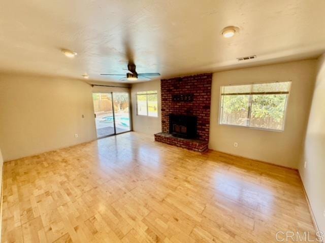 unfurnished living room featuring ceiling fan, a fireplace, a wealth of natural light, and light hardwood / wood-style flooring