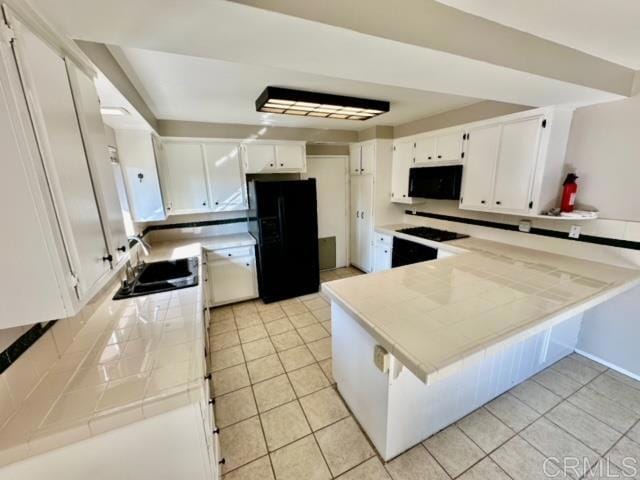 kitchen with sink, black appliances, light tile patterned floors, white cabinetry, and tile counters