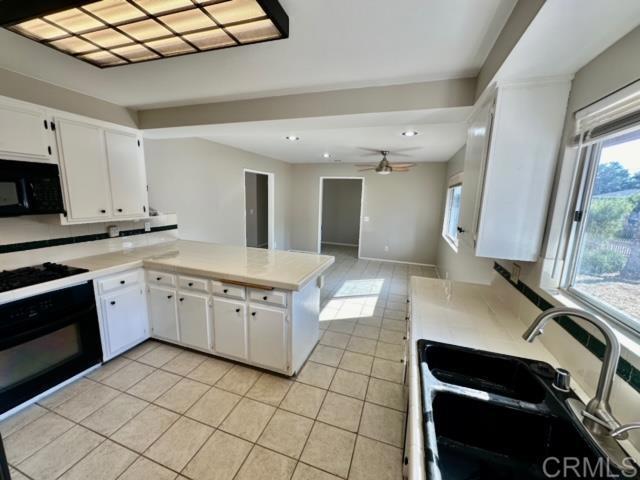 kitchen featuring black appliances, kitchen peninsula, sink, ceiling fan, and white cabinetry