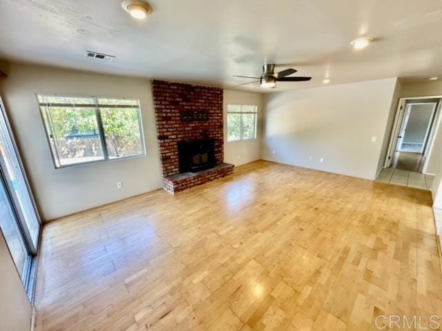 unfurnished living room featuring light hardwood / wood-style flooring, a brick fireplace, a wealth of natural light, and ceiling fan