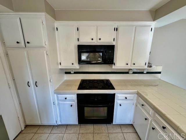 kitchen featuring backsplash, black appliances, light tile patterned floors, white cabinets, and tile counters