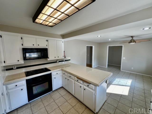 kitchen with black appliances, light tile patterned flooring, white cabinets, and kitchen peninsula