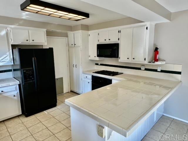 kitchen featuring light tile patterned floors, white cabinetry, tile counters, black appliances, and kitchen peninsula