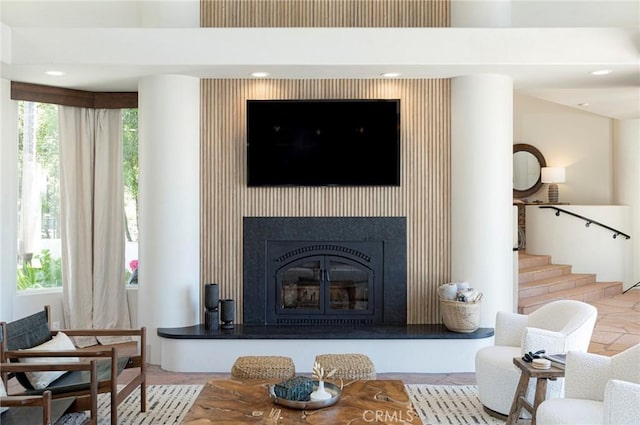 living area featuring stairs and a glass covered fireplace