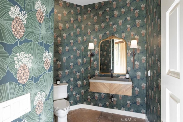 half bathroom featuring wallpapered walls, a sink, toilet, and baseboards