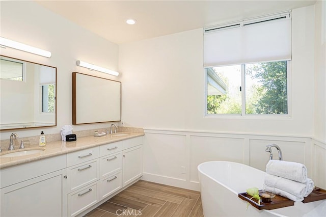 full bath with double vanity, a soaking tub, a sink, and recessed lighting