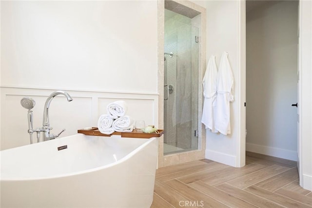 bathroom featuring a wainscoted wall, a soaking tub, a decorative wall, a shower stall, and baseboards