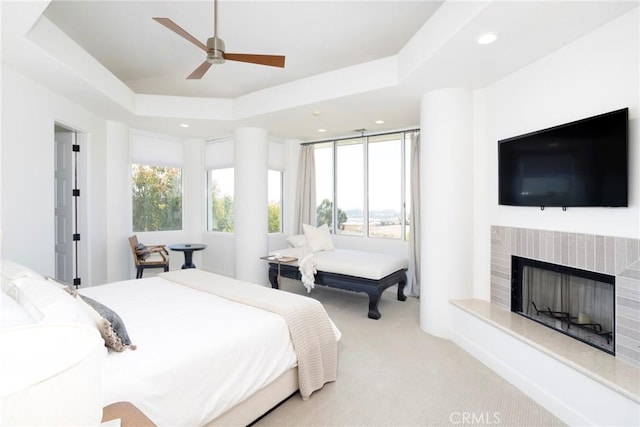 carpeted bedroom with a fireplace with raised hearth, ceiling fan, a raised ceiling, and recessed lighting