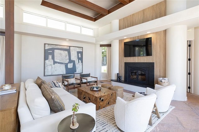 living room featuring stone tile flooring, a fireplace, a towering ceiling, and beam ceiling