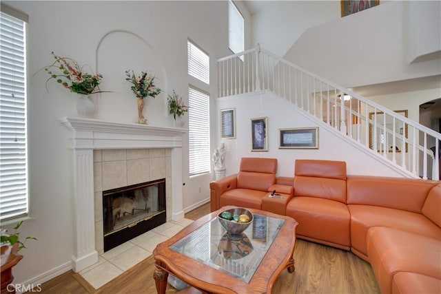 living room with a tiled fireplace, a high ceiling, and light hardwood / wood-style floors