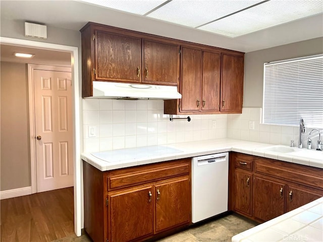 kitchen with decorative backsplash, white dishwasher, sink, light hardwood / wood-style flooring, and tile counters