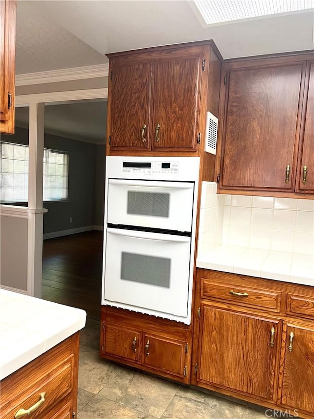 kitchen featuring tile countertops, white double oven, light hardwood / wood-style flooring, decorative backsplash, and ornamental molding