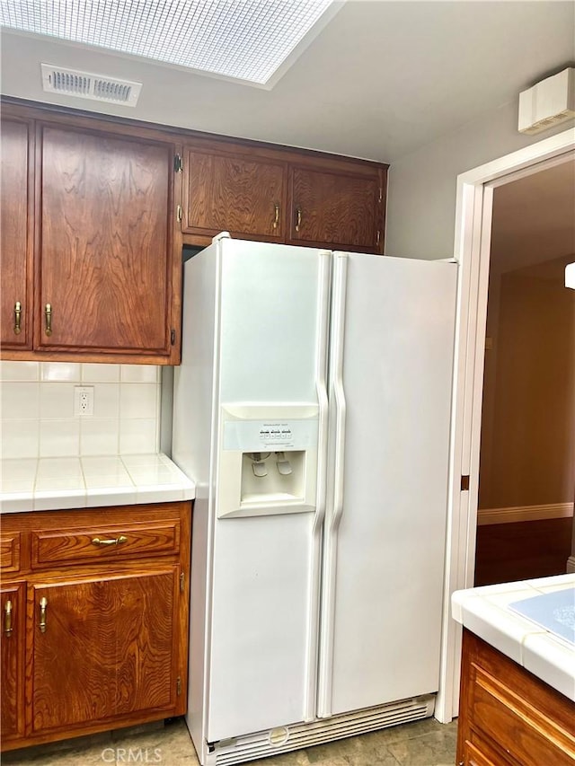 kitchen with tile counters, white refrigerator with ice dispenser, and tasteful backsplash