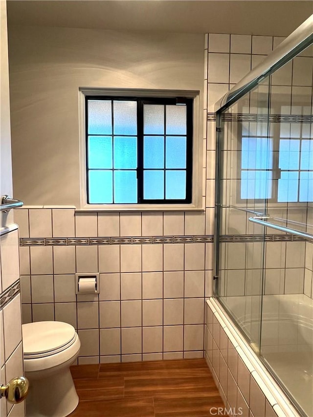 bathroom featuring hardwood / wood-style floors, toilet, a shower with shower door, and tile walls