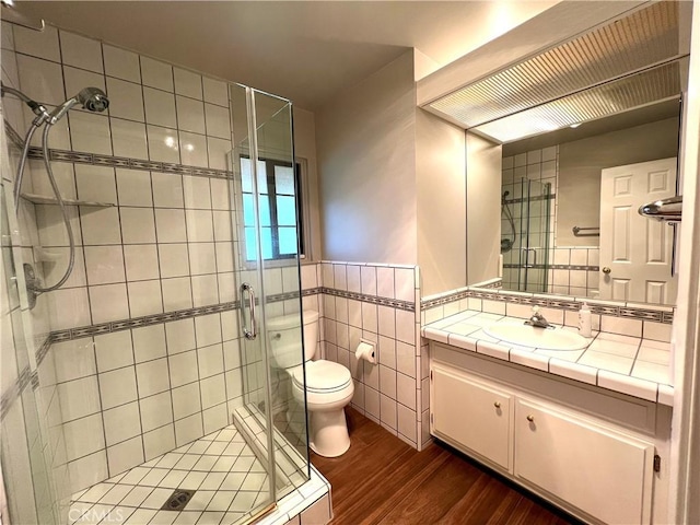 bathroom with vanity, hardwood / wood-style flooring, toilet, tile walls, and a shower with shower door