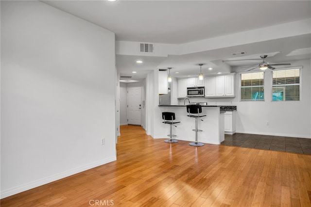 kitchen featuring hanging light fixtures, white cabinetry, a kitchen bar, and hardwood / wood-style flooring