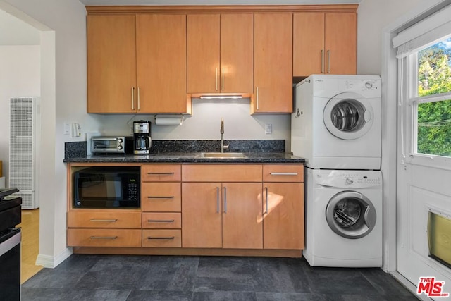 kitchen with stacked washer and dryer, dark stone counters, and sink