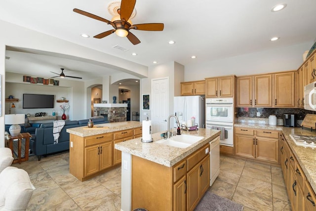 kitchen with white appliances, sink, ceiling fan, light stone counters, and a center island with sink